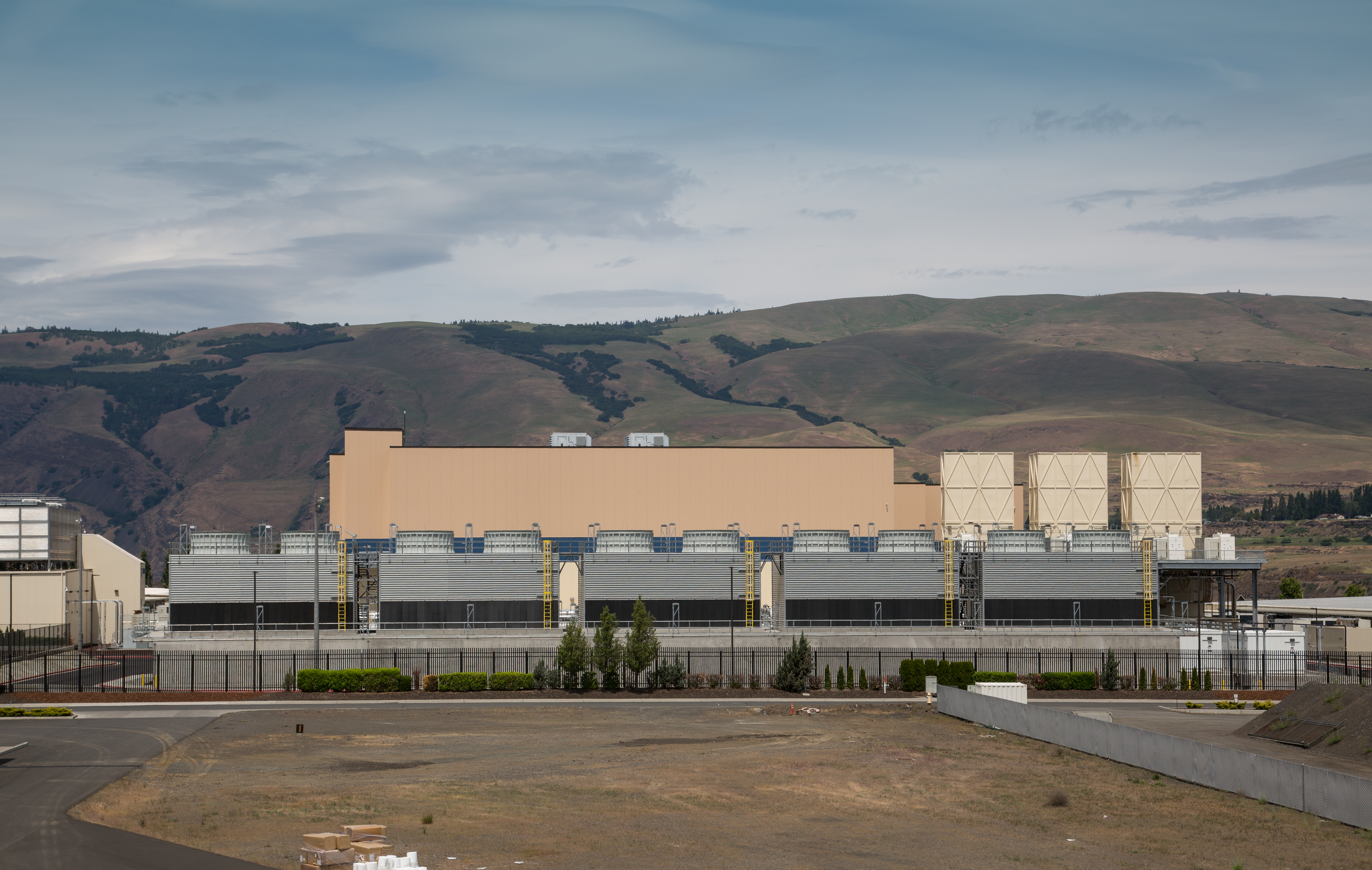 Google data center in The Dalles, Oregon, with a long row of cooling units in front of tan buildings and dry hills, photographed in 2015.
