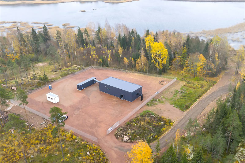 Aerial view of the Hamina heat pump plant in a cleared lot beside forest and water.